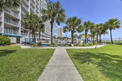 a sidewalk in front of a building with palm trees at PCB Condo with 2 Outdoor Pools and Beach Access! in Panama City Beach