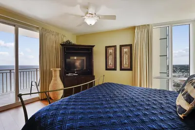 a bedroom with a bed and a tv and windows at Splash Beach Resort #1601-W by Book That Condo in Panama City Beach