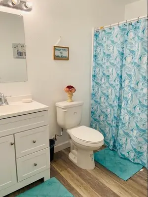 a bathroom with a toilet and a blue shower curtain at Peace On The Beach House in Panama City Beach