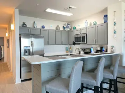 a kitchen with white cabinets and a counter with chairs at Calypso 3-2303 Penthouse Level w/ Incredible View! in Panama City Beach