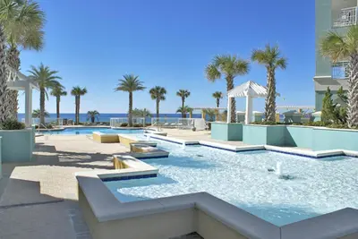 a pool at a resort with palm trees and the ocean at En Soleil Beach Resort by Panhandle Getaways in Panama City Beach