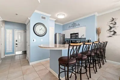 a kitchen with a bar with stools and a clock on the wall at Summer By The Sea Unit 2203 in Panama City Beach