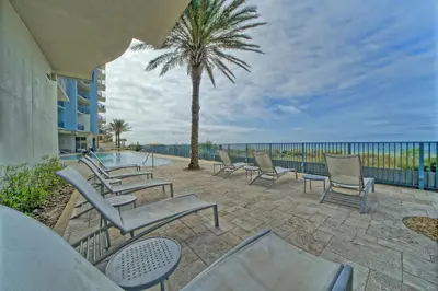a patio with chairs and a palm tree and the ocean at Sterling Breeze - Cozy Beachfront One Bedroom Condo in Panama City Beach