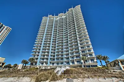 a tall building on the beach with palm trees at Sterling Breeze - Cozy Beachfront One Bedroom Condo in Panama City Beach