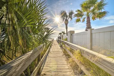 a wooden pathway with palm trees and a fence at The Sage PCB Family Getaway - Walk to Beach! in Panama City Beach