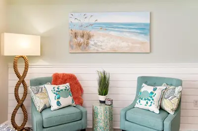 two chairs in a living room with a picture of a beach at Shores of Panama 2024 in Panama City Beach