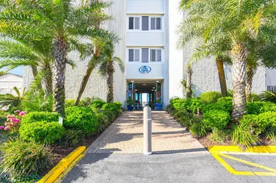 a building with palm trees in front of it at PCB Coastal Condo with On-Site Beach Access! in Panama City Beach