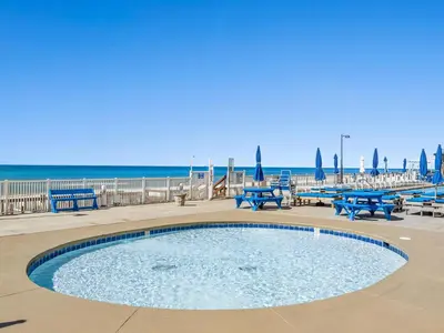 a swimming pool with blue benches and the beach at Regency Towers 505 in Panama City Beach