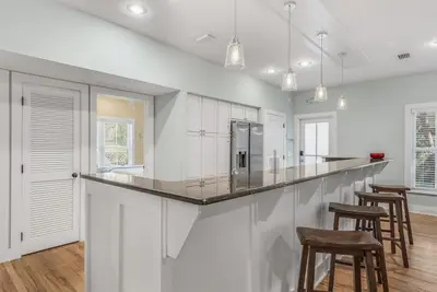 a kitchen with white cabinets and a bar with stools at Beach Bungalow, 3 Min Walk to Beach, Golf Cart, 4 bikes, Wagon in Seacrest