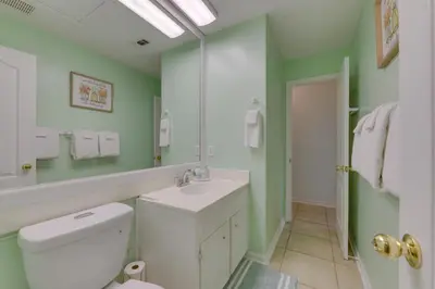 a bathroom with a toilet and a sink and a mirror at Cozy PCB Condo Less Than half Mile to Public Beach Access! in Panama City Beach