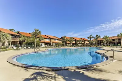 a swimming pool at a resort with palm trees and houses at Panama City Beach Townhome - Walk to Beach! in Panama City Beach