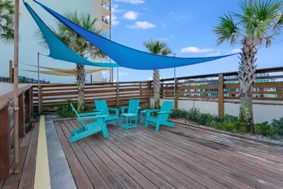 a deck with blue tables and chairs and palm trees at Top Of The Gulf 621 in Panama City Beach
