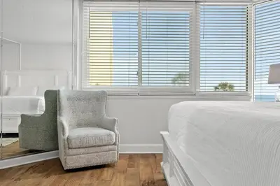 a white bedroom with a chair and a bed at Top of The Gulf 213 in Panama City Beach