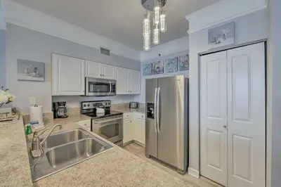 a kitchen with a stainless steel refrigerator and white cabinets at Oceanfront PCB Resort Condo with Balcony and Views! in Panama City Beach