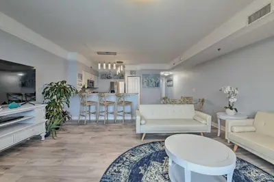 a living room with white furniture and a kitchen at Oceanfront PCB Resort Condo with Balcony and Views! in Panama City Beach