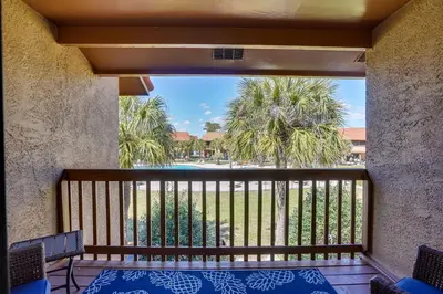 a balcony with a view of a pool and palm trees at Sun-Dappled PCB Retreat with Multiple Pools! in Panama City Beach
