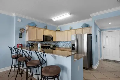 a kitchen with a bar with stools and a refrigerator at Ocean Villa 1101 in Panama City Beach