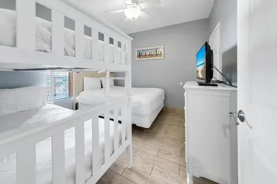 a white bedroom with two bunk beds and a tv at Splash 1802E in Panama City Beach