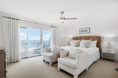 a white bedroom with a bed and a chair and a balcony at SeaRenity at Inlet 2 in Panama City Beach