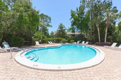 a large swimming pool with chairs and trees at Cassine Gardens 108- Sandy Daze in Santa Rosa Beach