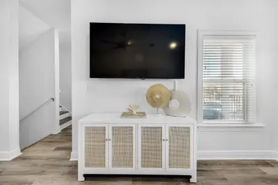 a white living room with a tv on a wall at Legacy 505- Pearl by the Sea in Santa Rosa Beach