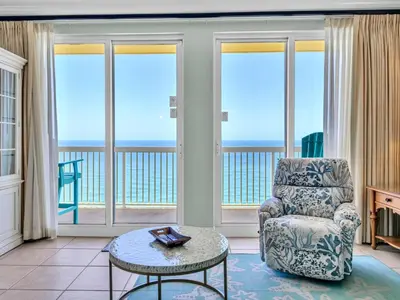a living room with a chair and a table and windows at Calypso 1-2109 East in Panama City Beach