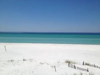 a white beach with a fence in front of the ocean at Beach Daze in Panama City Beach