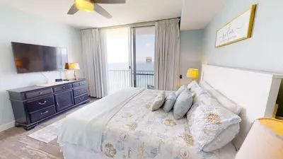 a bedroom with a bed with a television and a balcony at Tidewater 1909 in Panama City Beach