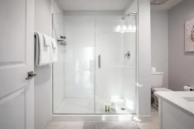 a white bathroom with a shower with a glass door at Modern Beach Vibe with a Breathtaking View - Stunning Pool - Pier Park in Panama City Beach