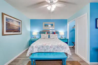 a blue bedroom with a bed and a ceiling fan at PCB Apt with Balcony and Gulf Views Walk to Beach in Panama City Beach