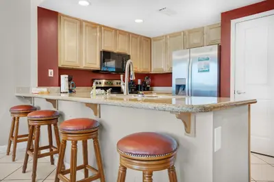 a kitchen with wooden cabinets and bar stools at Grandview East 404 in Panama City Beach