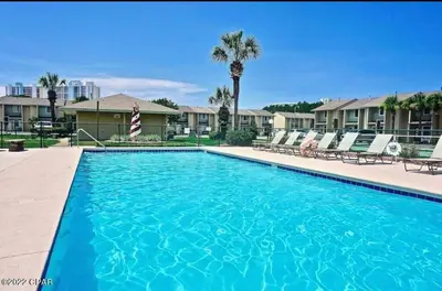 a large swimming pool with chairs and palm trees at Desirable Pet Friendly Resort, 3 minute walk to the Beach, Beachside Pool & Restaurant Message for Snow Bird Rates in Panama City Beach