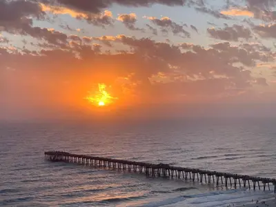 a pier in the ocean with the sunset in the background at Sunset Cove at Calypso III in Panama City Beach