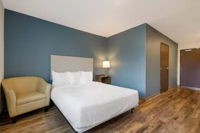 a bedroom with a white bed and a chair at WoodSpring Suites Panama City Beach in Panama City Beach