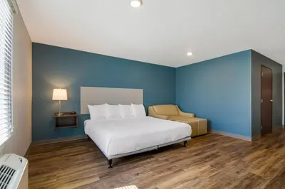 a bedroom with a white bed and a blue wall at WoodSpring Suites Panama City Beach in Panama City Beach
