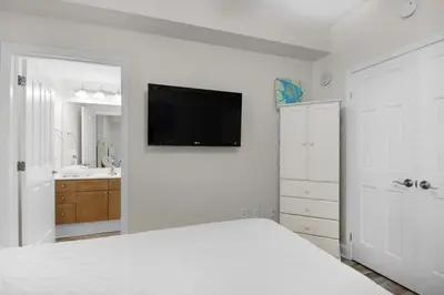 a white bedroom with a bed and a tv on the wall at Aqua Resort 2103 in Panama City Beach