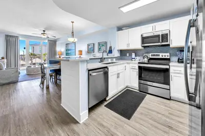 a kitchen with white cabinets and a table with a sink at Calypso 3-202 - The Sea Suite in Panama City Beach