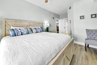 a bedroom with a large bed and a blue chair at Calypso 3-202 - The Sea Suite in Panama City Beach