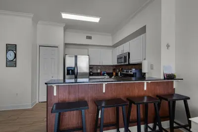 a kitchen with three bar stools and a refrigerator at Tidewater 3013 in Panama City Beach