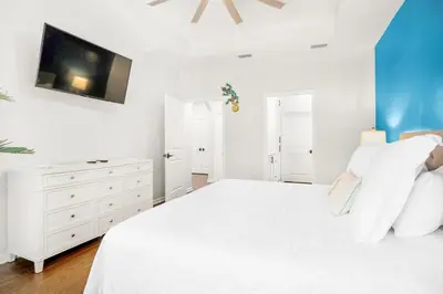 a white bedroom with a white bed and a tv at Pearl Flamingo in Panama City Beach