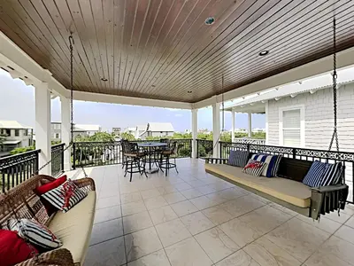 a porch with swings and a table and chairs at Seabreeze Cabana in Rosemary Beach