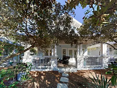a white house with a porch and a tree at The Good Life in Seacrest