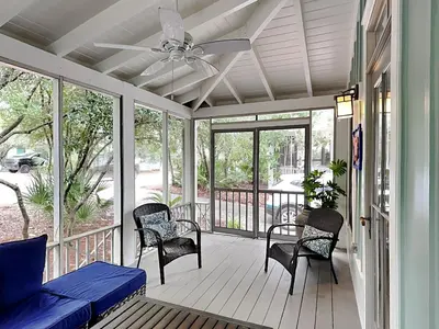 a screened porch with chairs and a couch and a ceiling fan at Sand Piper in Seacrest