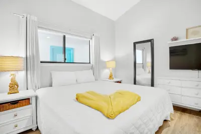 a white bedroom with a bed with a yellow blanket on it at Nautical Watch A-11 in Panama City Beach