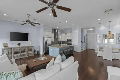 a living room with white furniture and a kitchen at Prominence 30A - Coastal Cottage in Panama City Beach