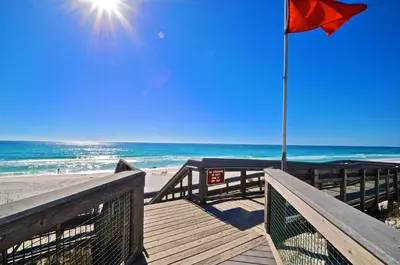 a boardwalk leading to the beach with a red flag at Prominece 30A - Coasting Inn in Watersound Beach