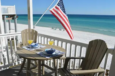 a table and chairs with an american flag and the beach at Beach Happy - Gulf Front in Santa Rosa Beach