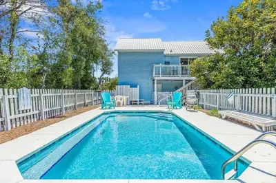 a swimming pool with blue chairs and a house at High Cotton Beach Cottage in Inlet Beach