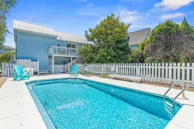 a swimming pool with two blue chairs and a house at High Cotton Beach Cottage in Inlet Beach