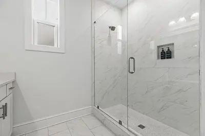 a white bathroom with a shower with a glass door at Crabbing Hole Lane in Rosemary Beach